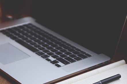 A notebook computer next to paper and a pen.